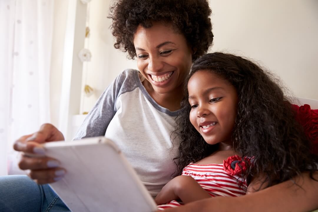 Mother and daughter smiling and looking at a tablet.