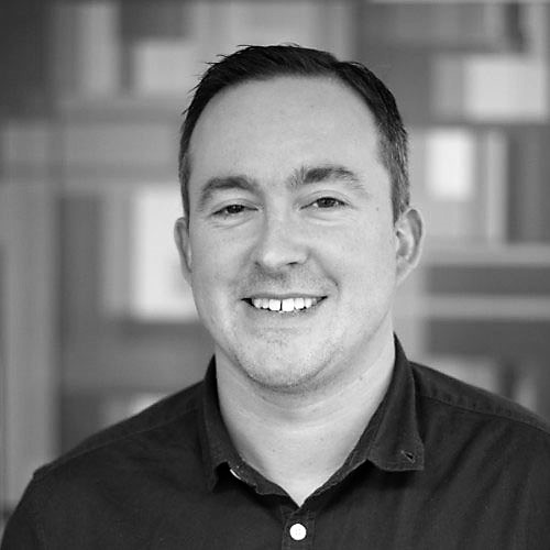 Black and white headshot of a man smiling with a shirt on called Simon Barratt